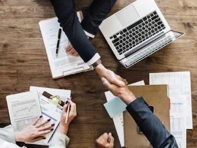 businessmen shaking hands over paperwork and laptop