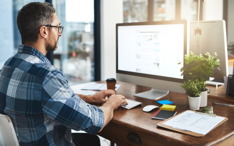 man sitting at a desk on typing on an imac keyboard in an office - tungsten network total ap
