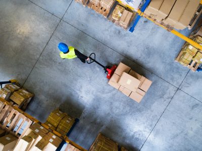 Young male warehouse worker pulling a pallet truck with boxes. Aerial view.