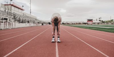 Keeping up with tax compliance symbolized by male runner bent over, hands on knees, looking tired, on running track
