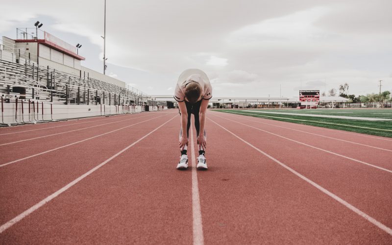 Keeping up with tax compliance symbolized by male runner bent over, hands on knees, looking tired, on running track